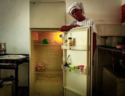 Pessoa ao lado de uma geladeira com poucos alimentos